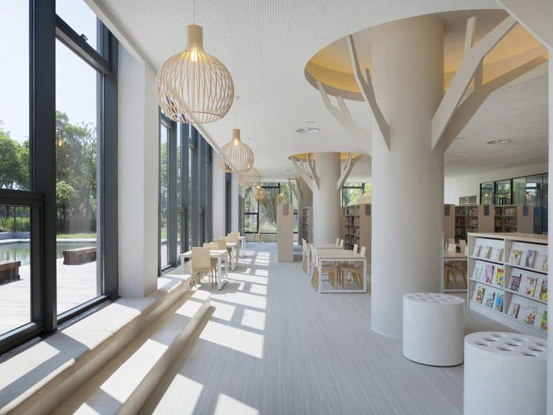 Bibliotheek met boomvormige kolommen en een lichte vloer langs een glazen gevel
