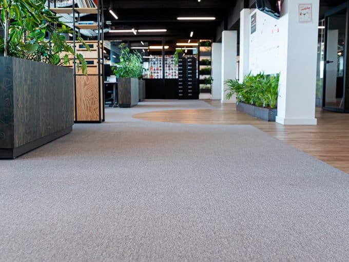 Kantoorvloer waar grijs tapijt overgaat in een houtkleurige vloer, met plantenbakken erlangs