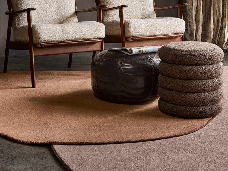 Rond terracotta karpet op een betonvloer, met twee fauteuils, een leren poef en een stapel zitkussens